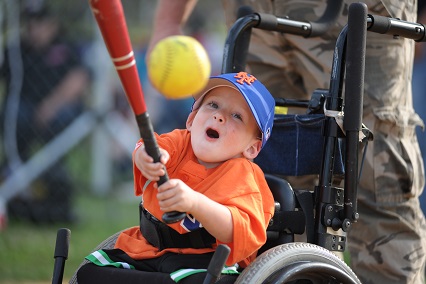 A joyful young boy in a wheel chair hits a baseball with a bat.