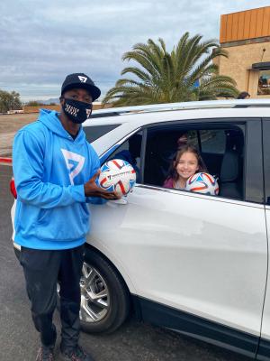 A man wearing a mask and holding a soccer ball stands next to a young girl holding a soccer ball