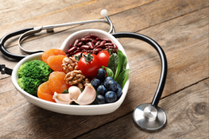 Heart shaped bowl fill with fruits and vegetables, and a stethoscope around the bowl.