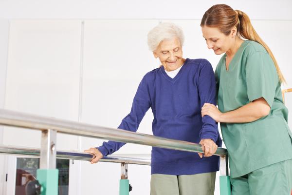 Una profesional de la salud ayuda a una mujer adulta mayor a hacer ejercicios de caminar.