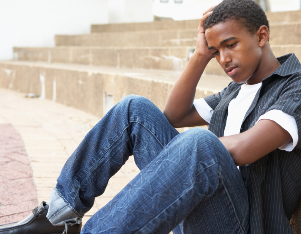 Teenage boy sitting on the ground with his head in his hand