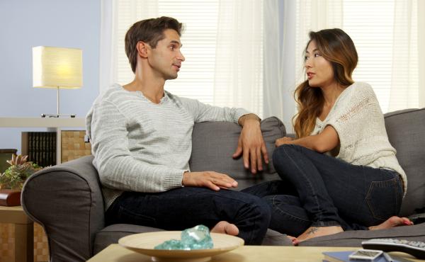 Una pareja (un hombre y una mujer) conversan en un sofá.