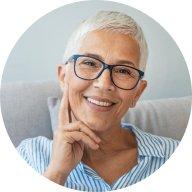 Woman with gray hair smiles and wears glasses and a blue shirt