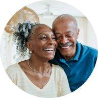 An older black woman and man smile as they stand cheek to cheek. 