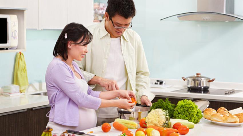 Man and pregnant woman preparing healthy produce for a meal.