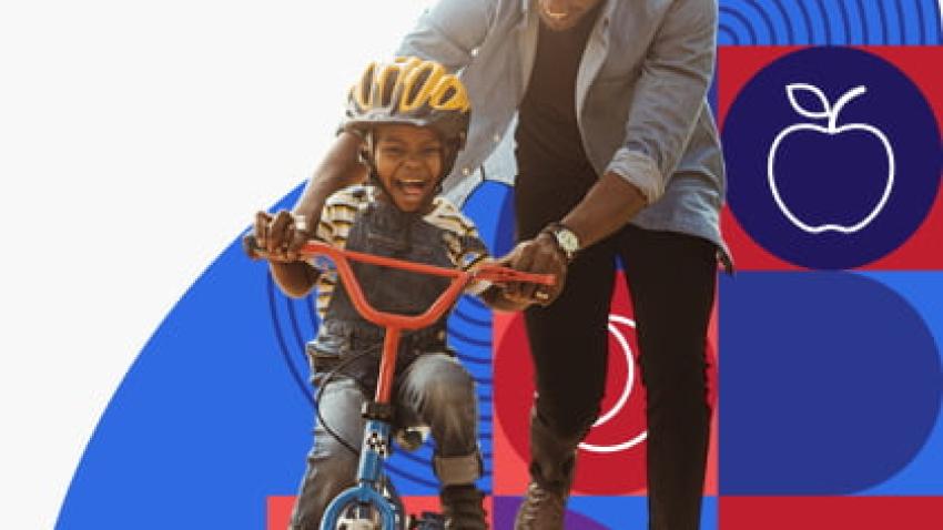 A child rides a bicycle while his dad holds onto the handlebars. 
